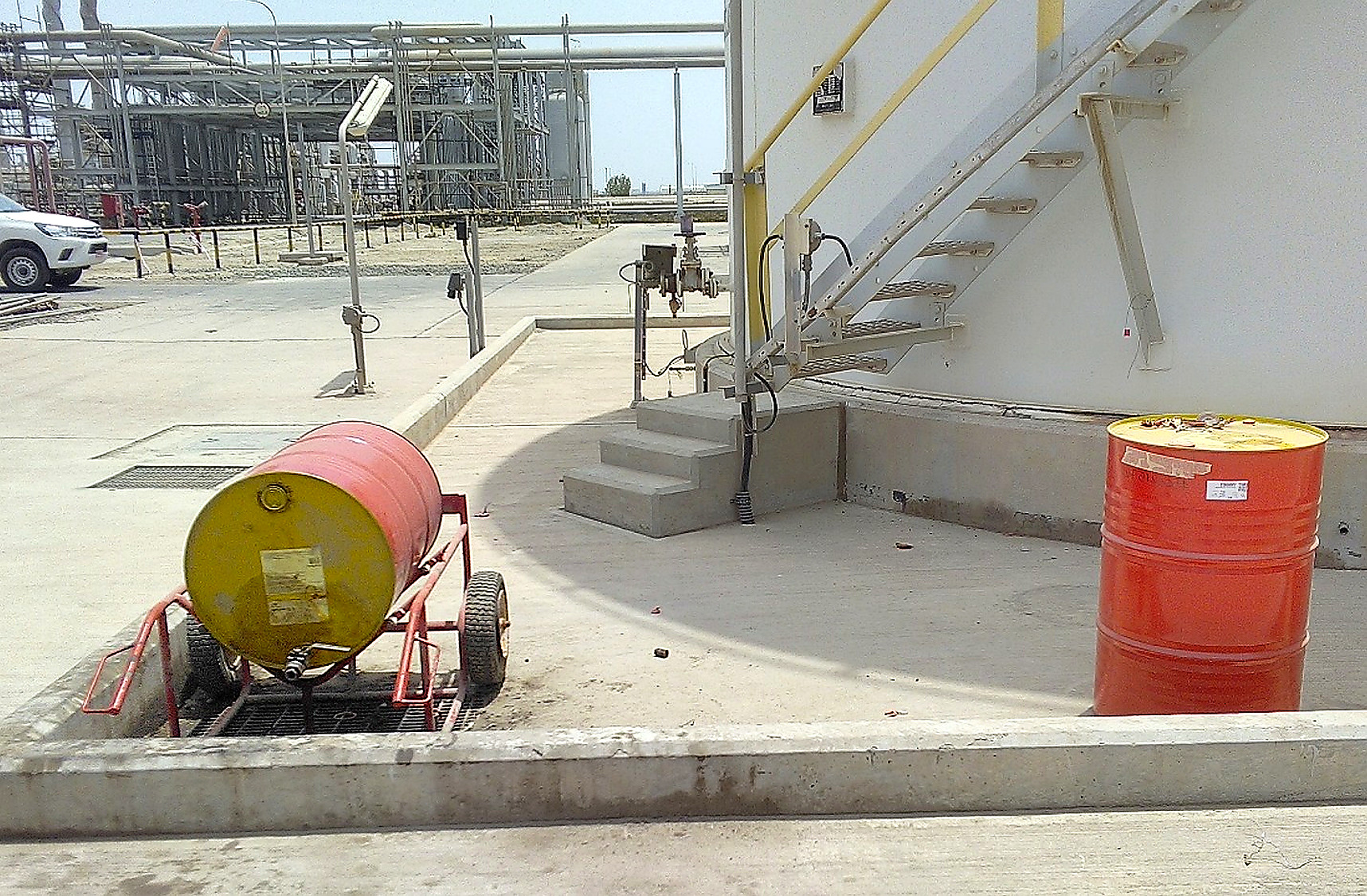Lubricant oil drums stored outdoors without cover or containment at an industrial site, directly exposing the oil to heat, dust, and moisture contamination