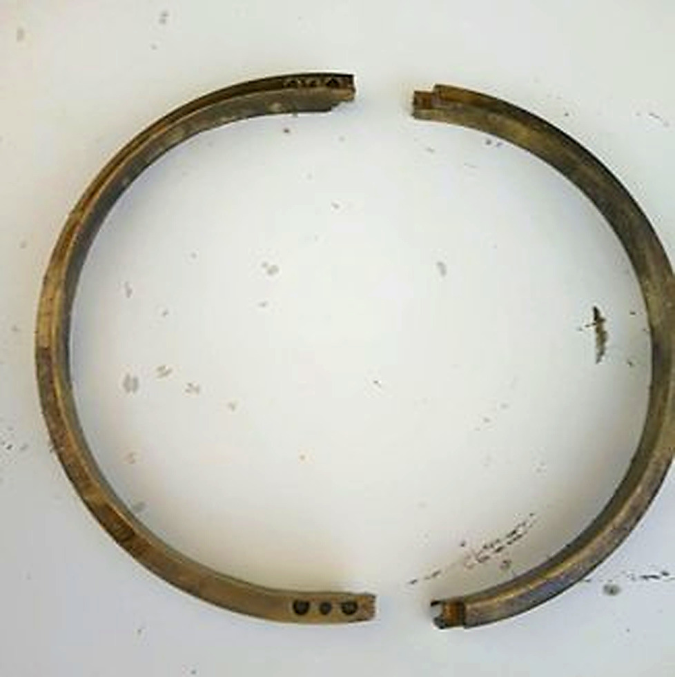 Oil ring broken into two separate halves laid flat, showing fatigue fracture and uneven wear from unstable rotation in degraded lubricant conditions